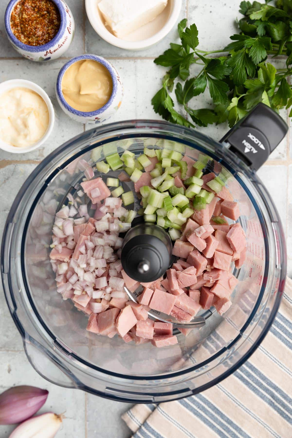 overhead photo of chopped ham, celery, and shallots in the bowl of a food processor