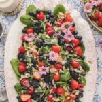 overhead of spinach berry salad on an ivory oval platter, garnished with pink edible flowers