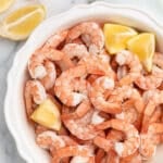 overhead of poached shrimp in a white fluted pie plate on a marble board with lemon wedges