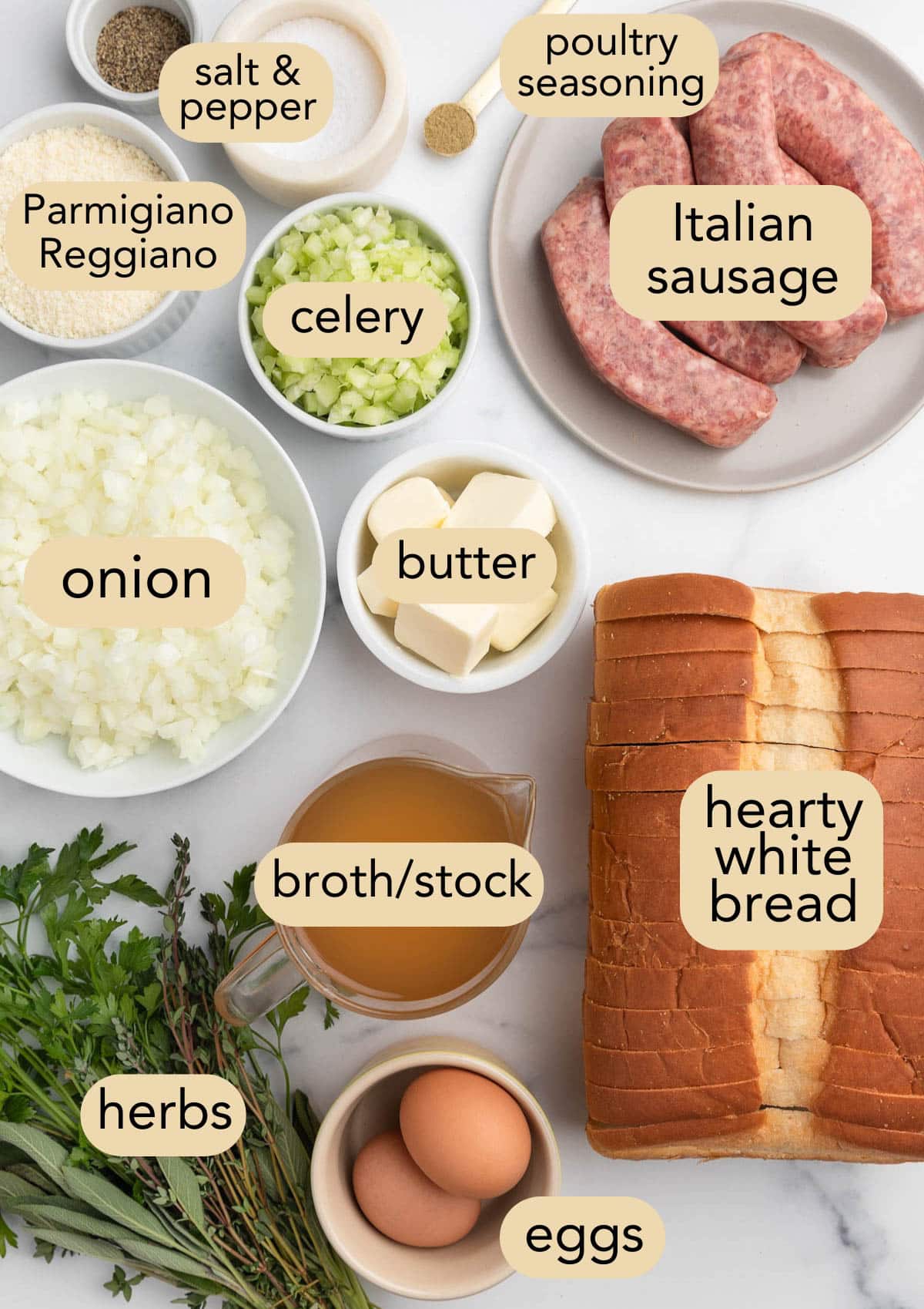 overhead of ingredients needed to make sausage stuffing in bowls on a white marble board with text labels
