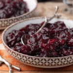 port cranberry sauce in a brown and white patterned bowl with a silver branch motif spoon on an orange damask napkin
