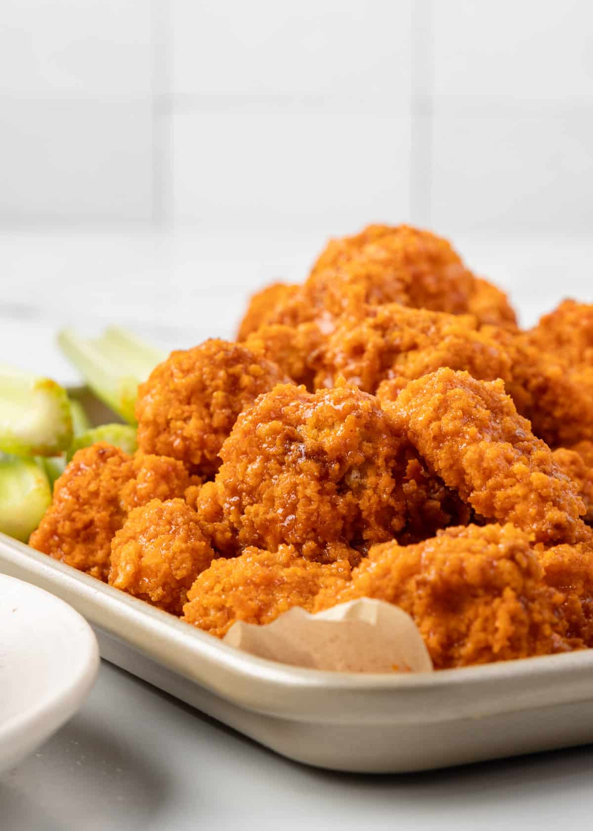 air fryer buffalo chicken piled onto a parchment lined baking sheet with celery sticks behind them