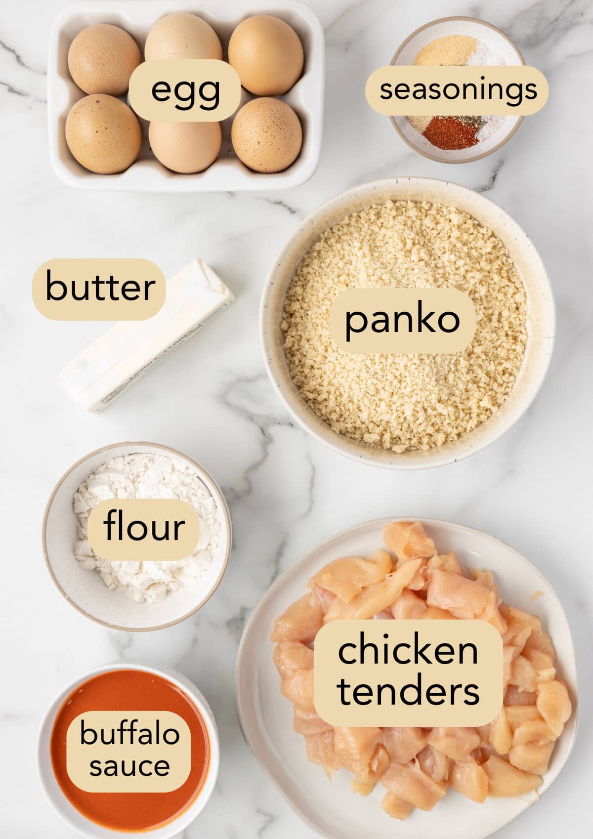 overhead of ingredients needed to make air fryer buffalo chicken bites in bowls on a white marble board with text label overlays