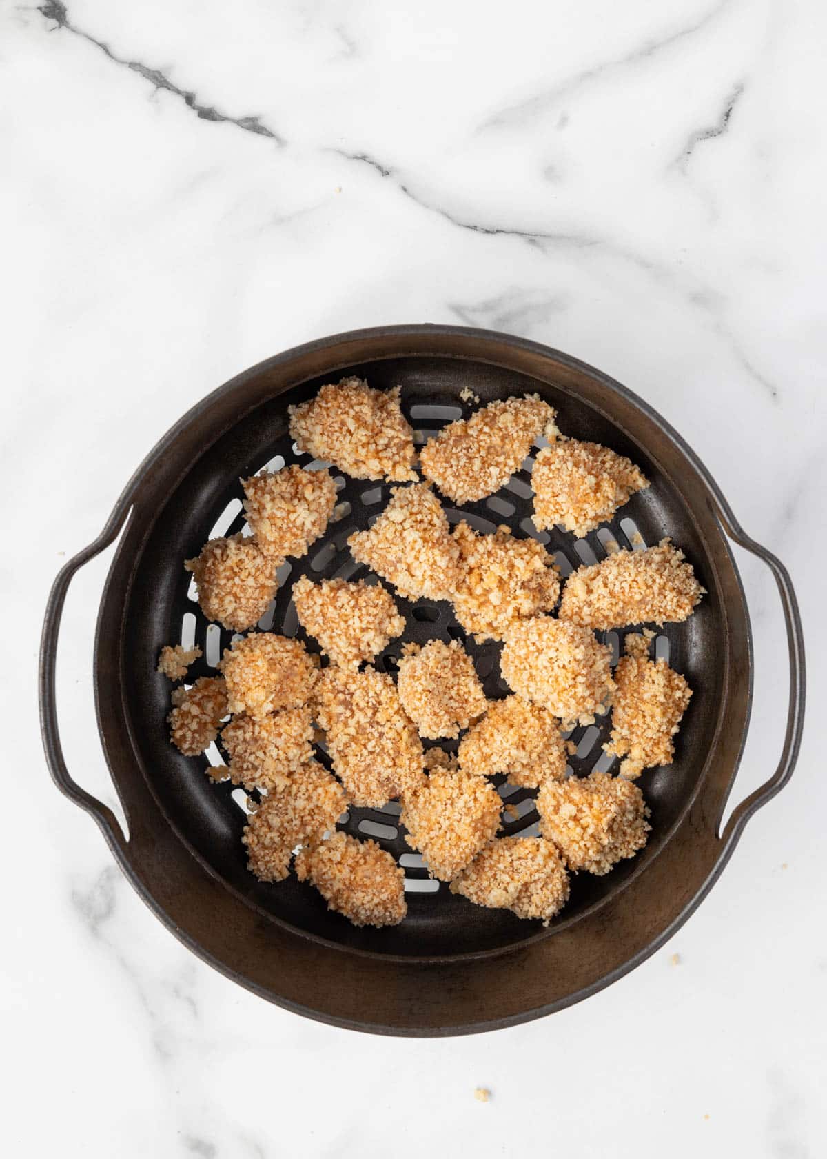 uncooked breaded buffalo chicken bites in an air fryer basket on a white marble board