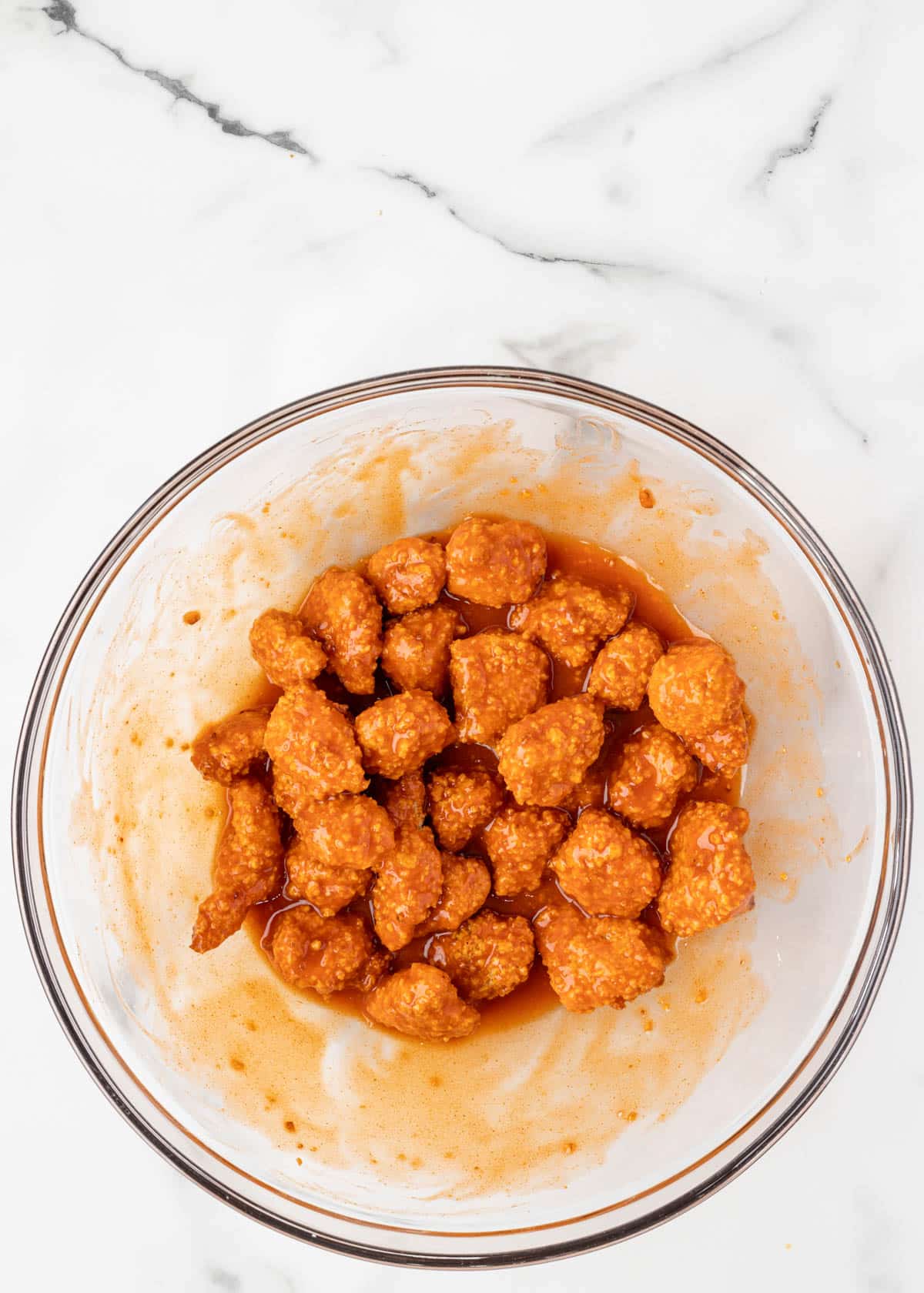 air fried buffalo chicken bites tossed in buffalo sauce in a glass bowl on a white marble board