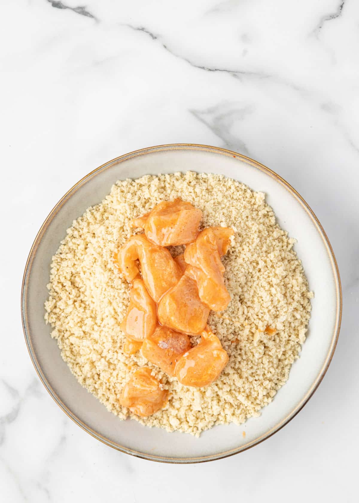 egg washed boneless chicken cubes in a bowl of seasoned panko breadcrumbs in a white marble board
