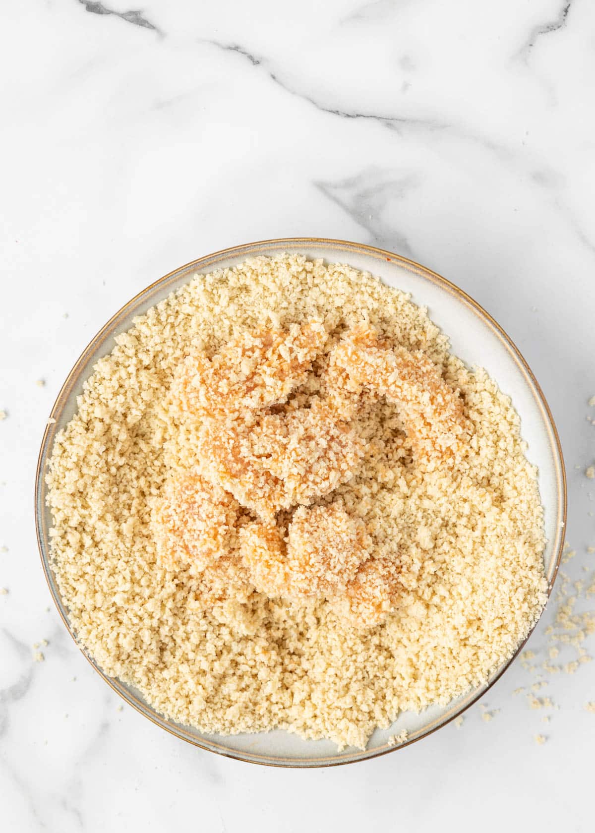 boneless chicken cubes breaded in seasoned panko in a bowl on a white marble board