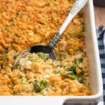 chicken broccoli rice casserole in a white baking dish with a silver serving spoon