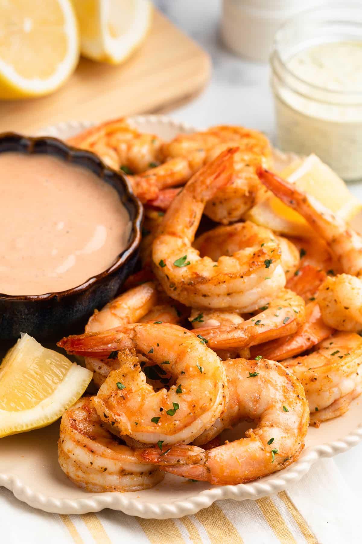 air fryer shrimp on an ivory scalloped plate with lemon wedges and a bowl of dipping sauce