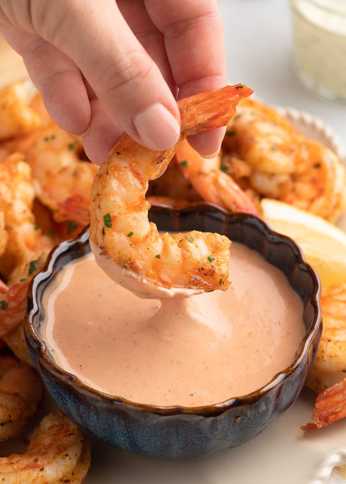 an air fried shrimp being dipped into a bowl of comeback sauce on a platter of shrimp with lemon wedges