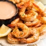 air fryer shrimp on an ivory scalloped plate with lemon wedges and a bowl of dipping sauce