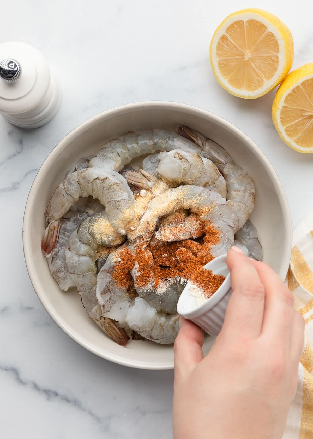 sprinkling ground spices over a bowl of raw shrimp from a tiny white ramekin