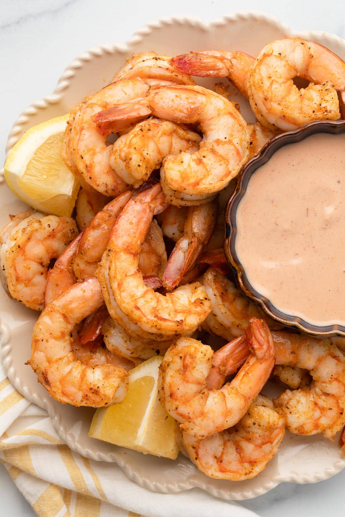overhead of a platter of air fryer shrimp with lemon wedges and a bowl of dipping sauce