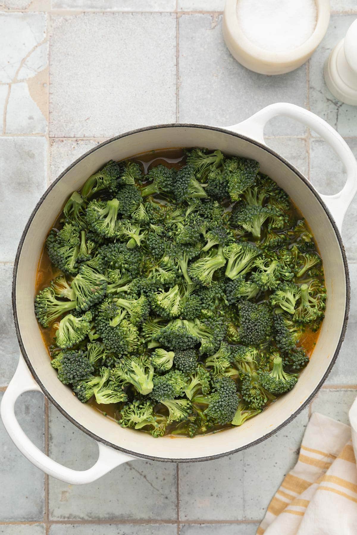 raw broccoli florets added to soup in a white enameled cast iron dutch oven