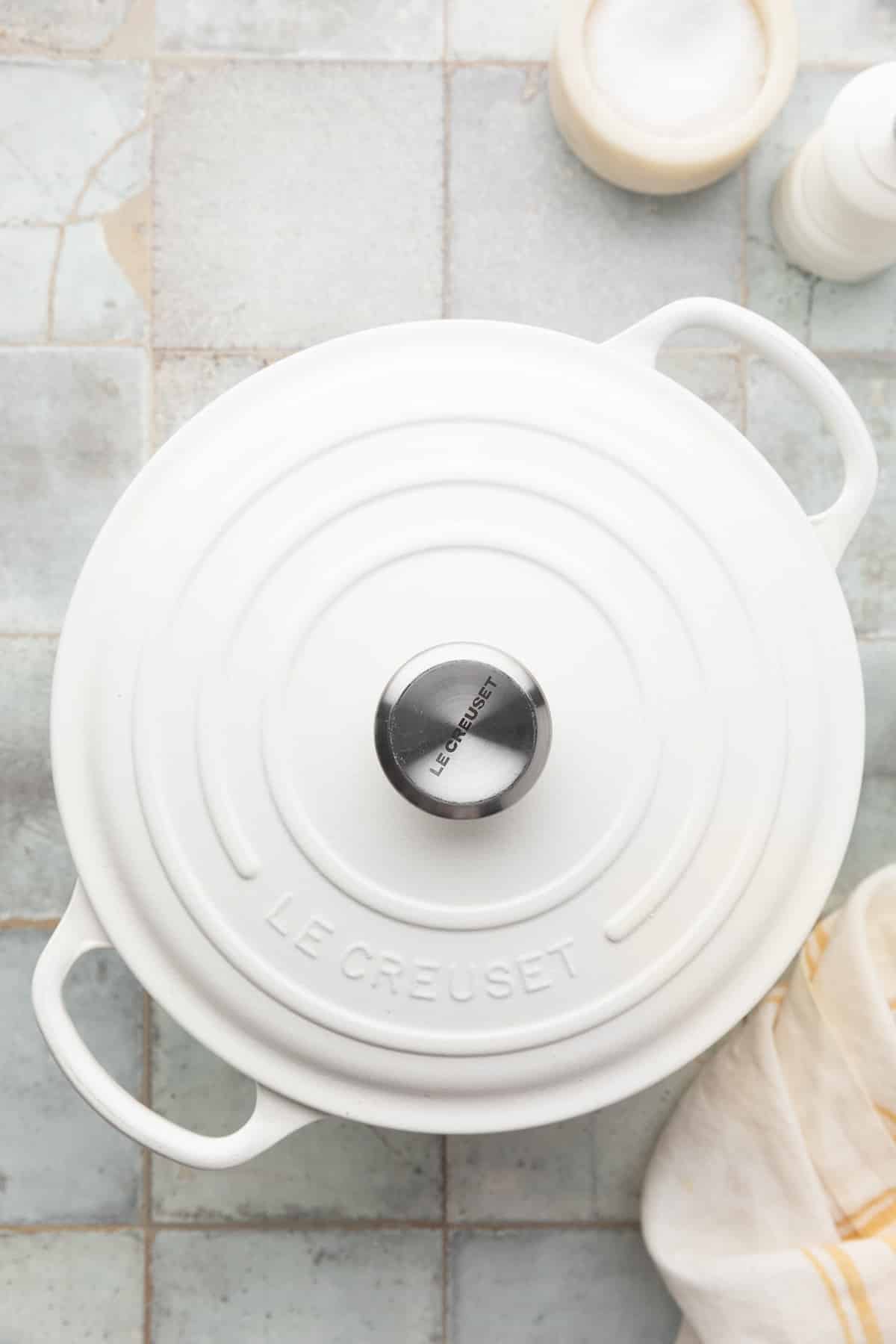 a covered white enameled cast iron dutch oven on a gray tile surface