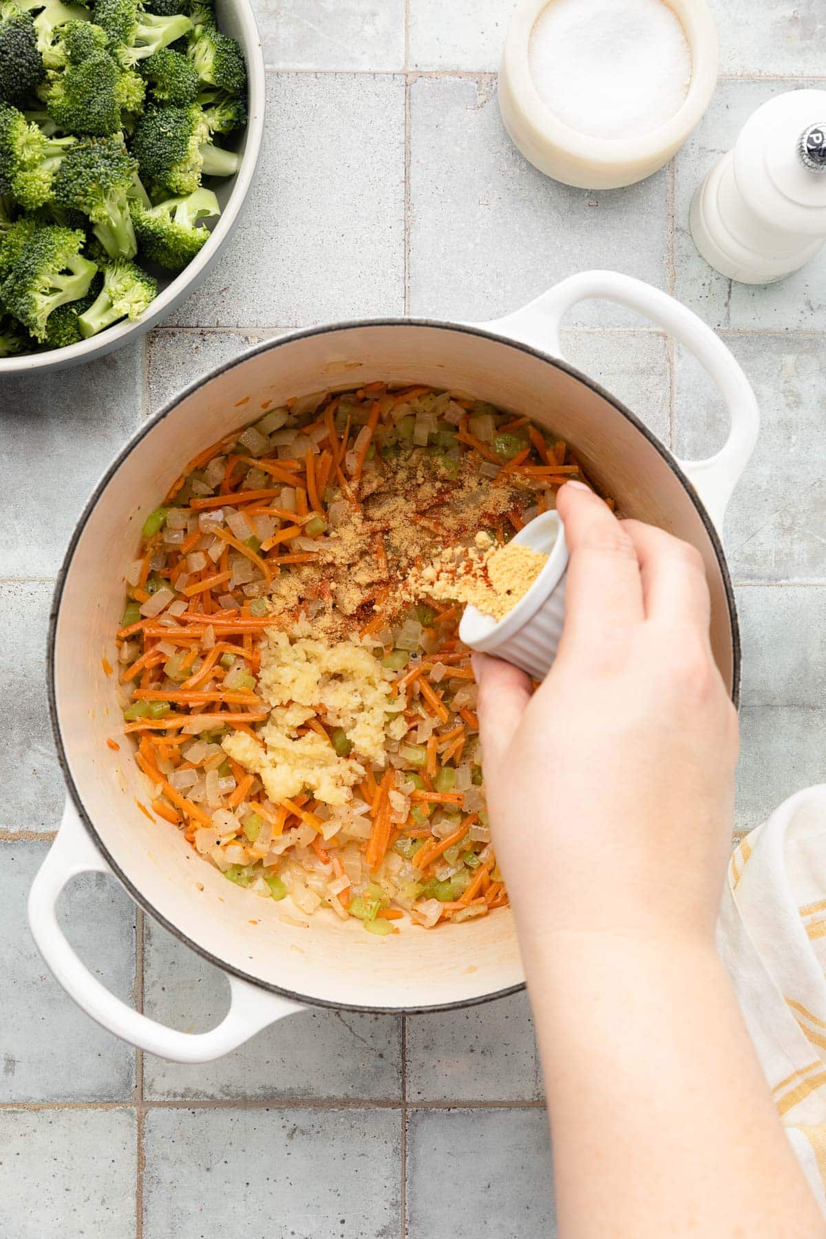 adding ground spices to sauteed carrots, onions, and celery in a white enameled cast iron dutch oven