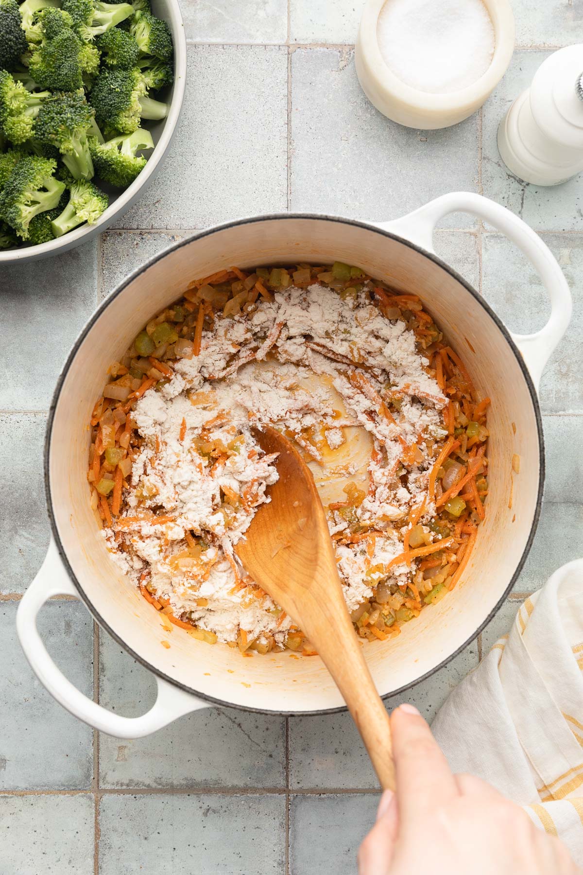 stirring flour into sauteed mirepoix in a white enameled cast iron dutch oven with a wooden spoon