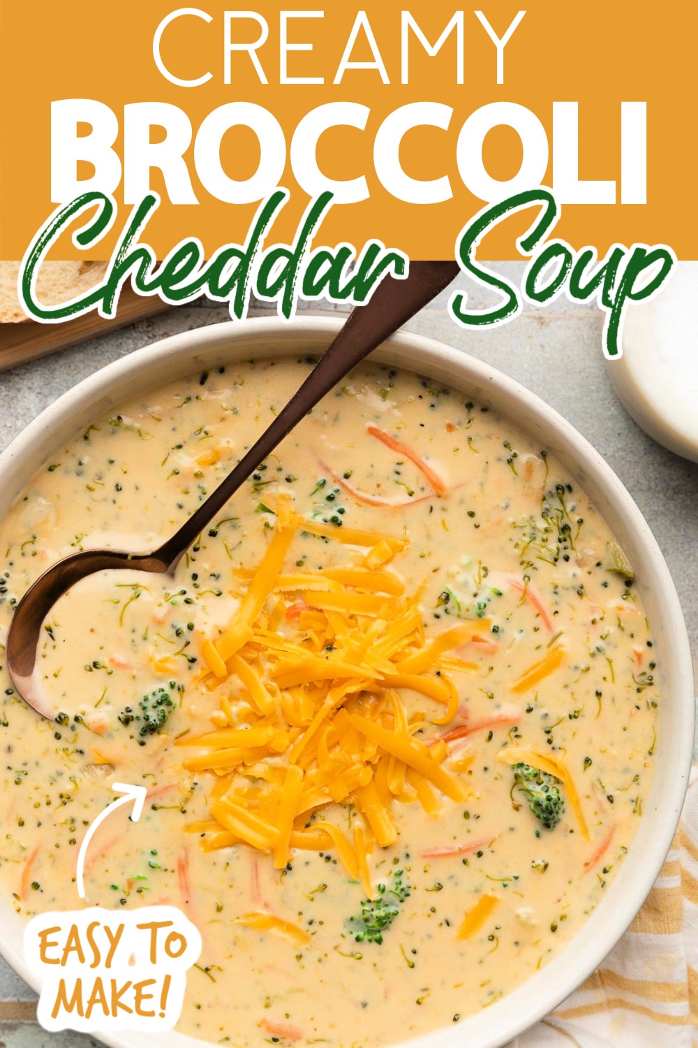 overhead of broccoli cheddar soup in an ivory ceramic bowl with a bronze soup spoon next to slices of crusty bread and a yellow and white striped napkin. Text reads "Creamy Broccoli Cheddar Soup" "Easy to Make!"