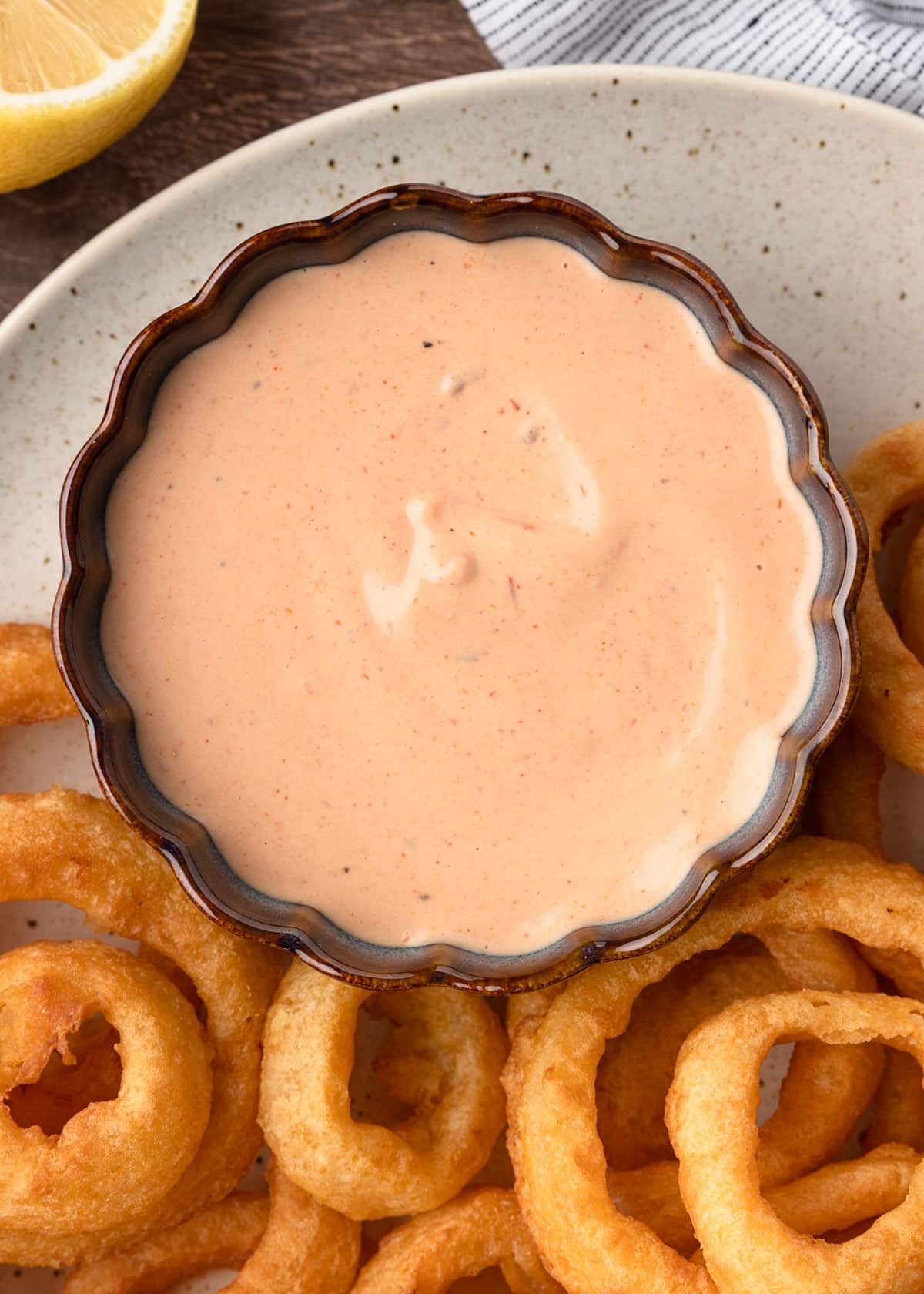 overhead of comeback sauce in a blue scalloped bowl on a platter of onion rings