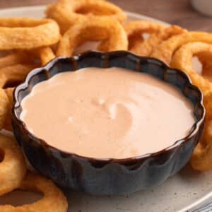 comeback sauce in a blue scalloped bowl on a plate of onion rings