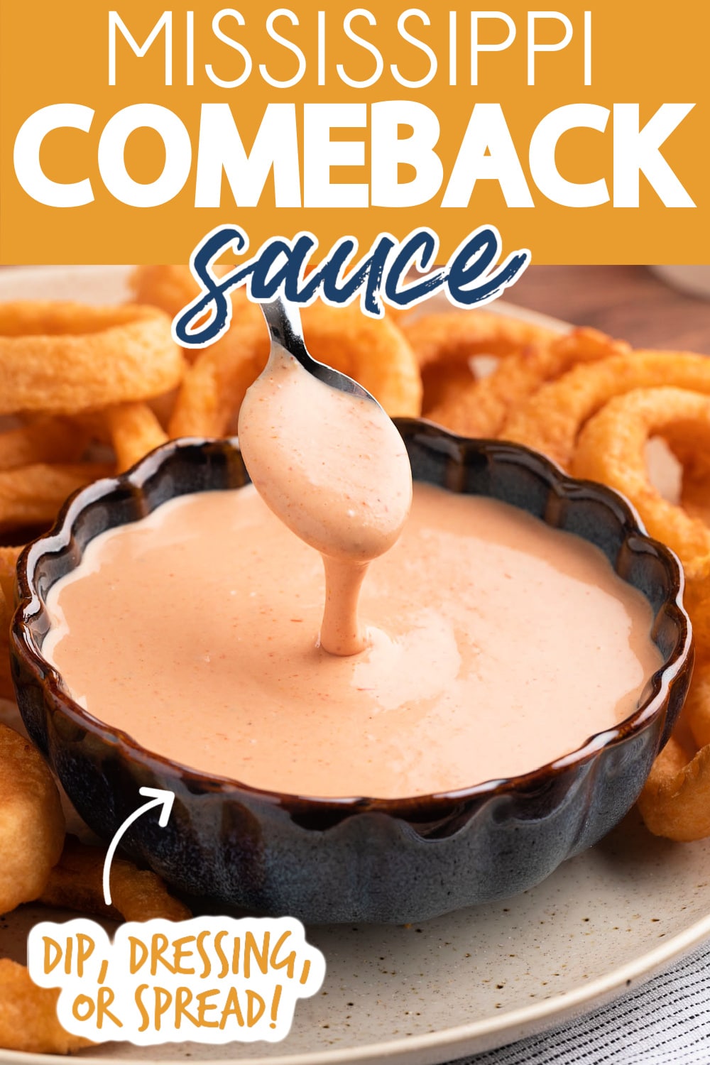 A spoonful of Comeback Sauce drizzling into a blue scalloped bowl filled with the sauce, on a platter with onion rings. Text reads "Mississippi Comeback Sauce" "Dip, Dressing, or Spread!"