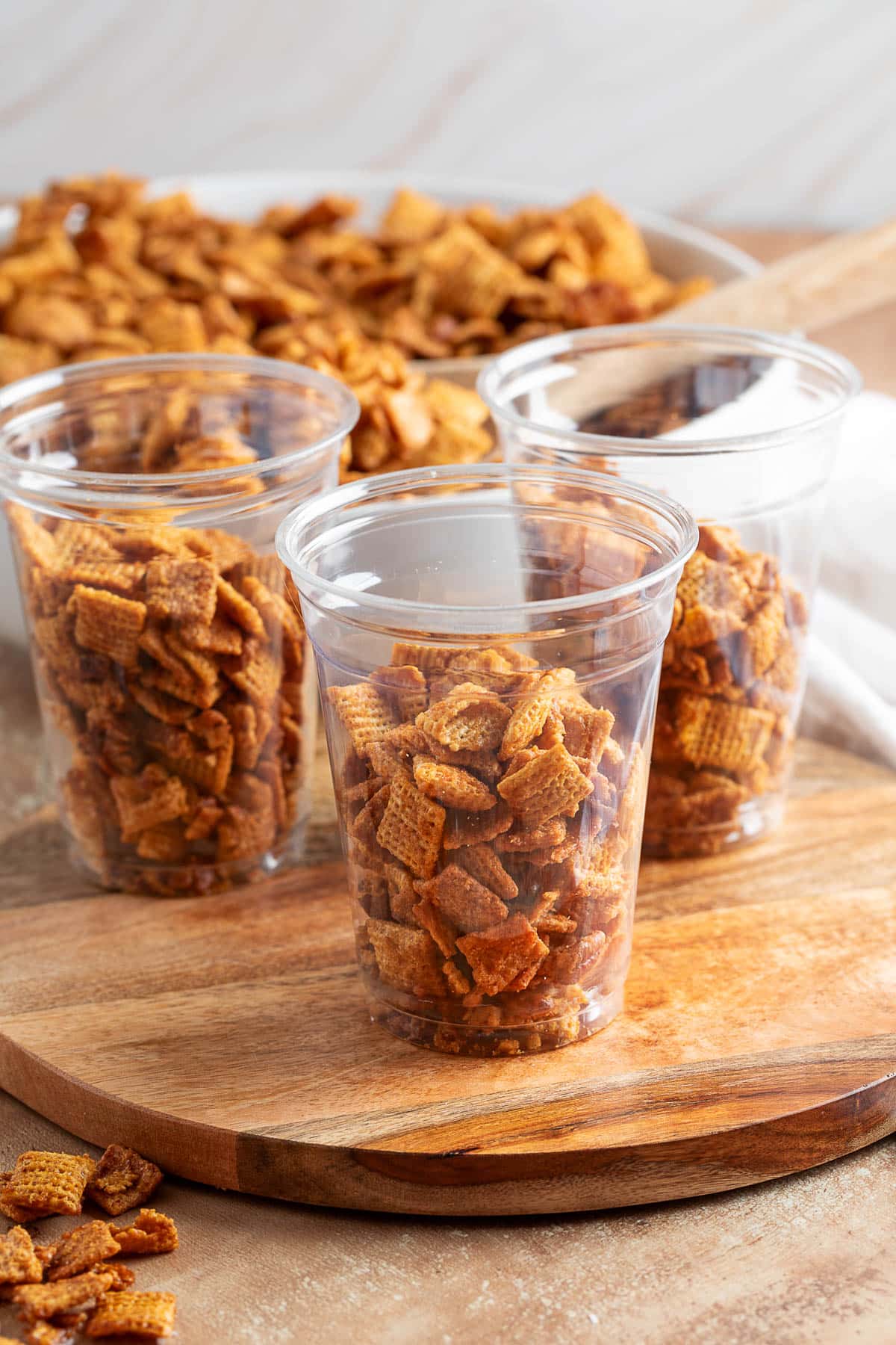 cinnamon praline crunch snack mix in clear plastic cups on a wood board