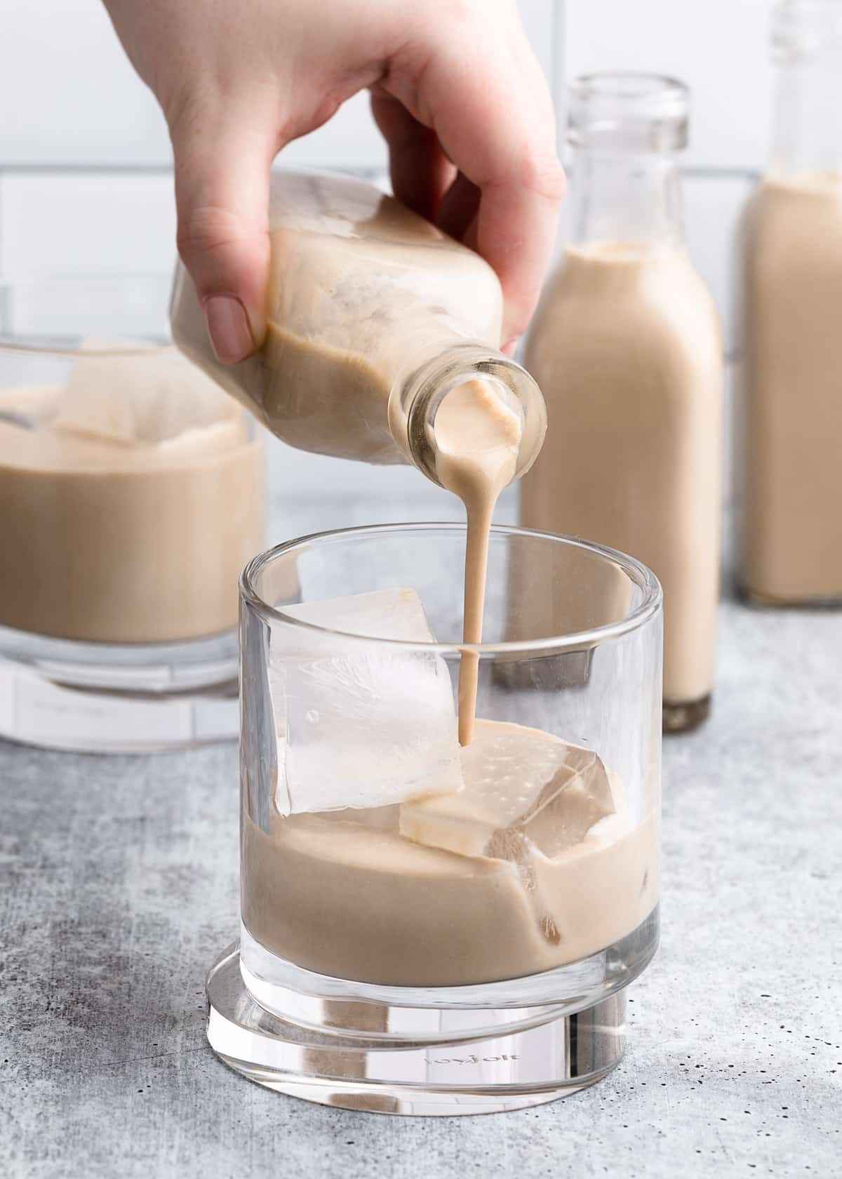 pouring homemade Irish Cream from a small glass bottle into a glass with ice