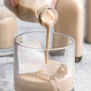 pouring homemade Irish Cream from a small glass bottle into a glass with ice