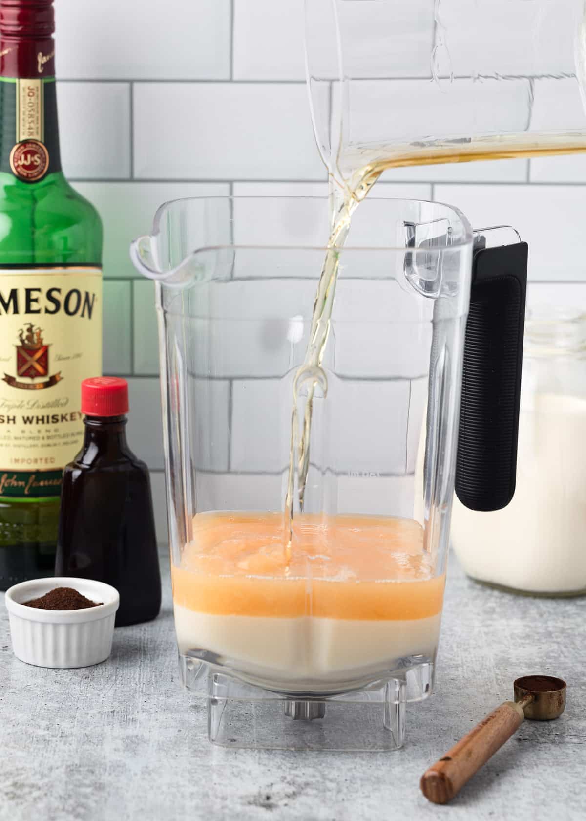 Irish whiskey being poured into a blender canister containing sweetened condensed milk