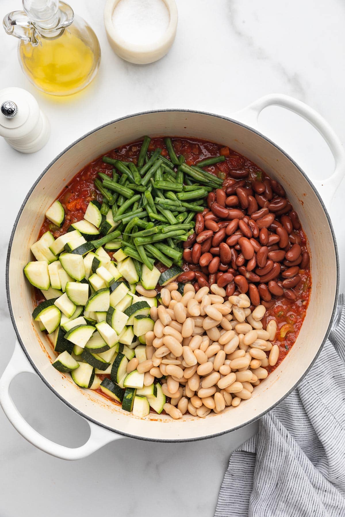 piles of zucchini, green beans, kidney beans, and cannellini beans added to a pot of uncooked minestrone soup