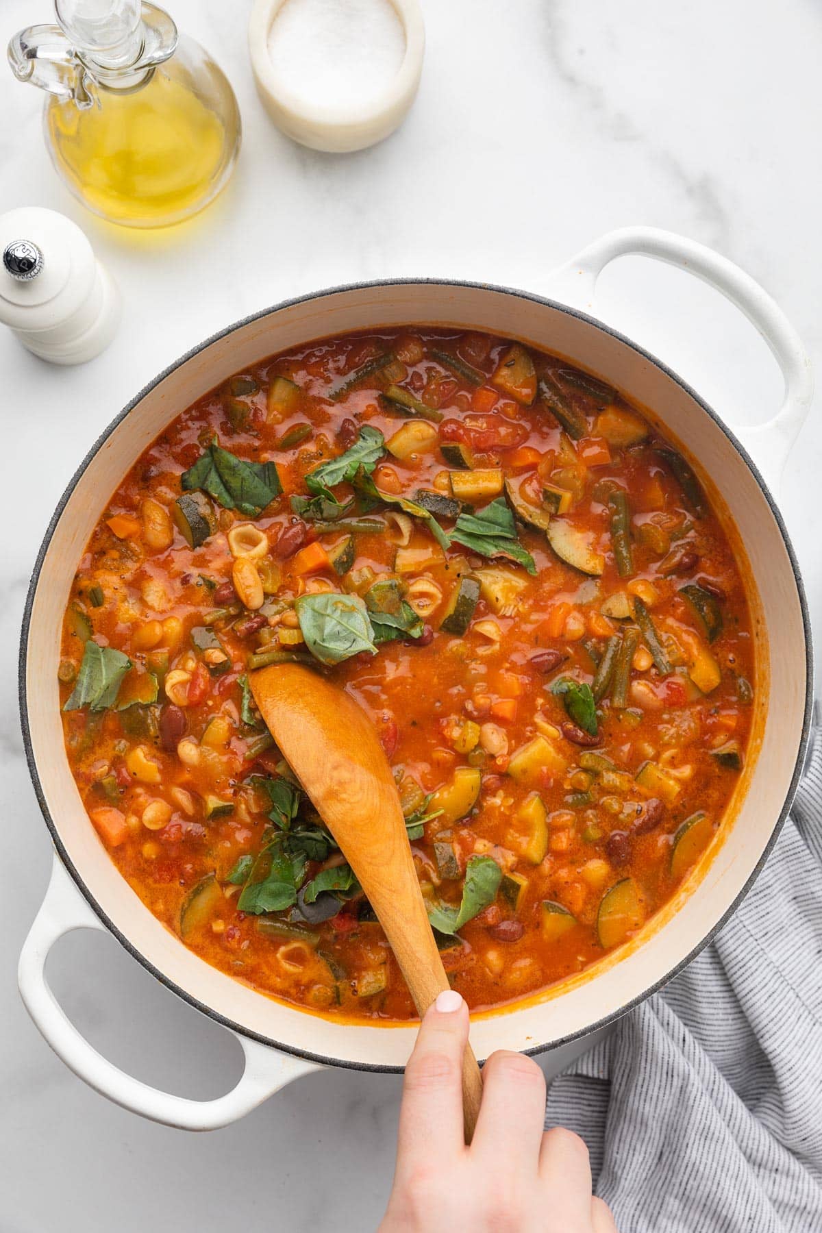 stirring torn basil leaves into a pot of minestrone soup with a wooden spoon