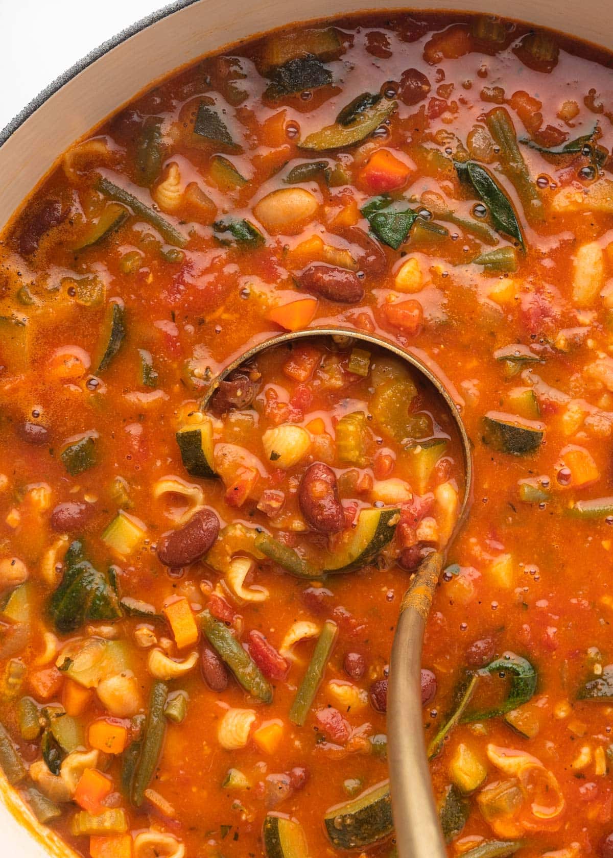 closeup overhead of minestrone soup being ladled from a pot
