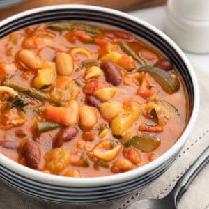 minestrone soup in a blue and white striped bowl on a taupe napkin