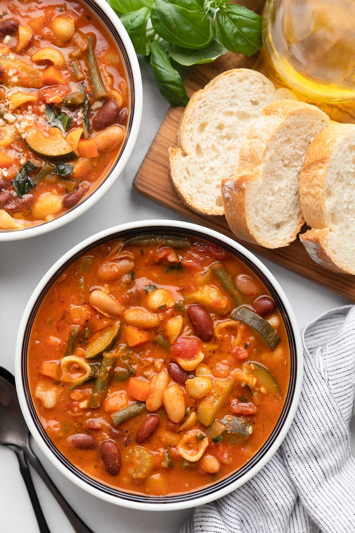 overhead of two bowls of minestrone soup in a white marble board with a bread board of sliced Italian bread
