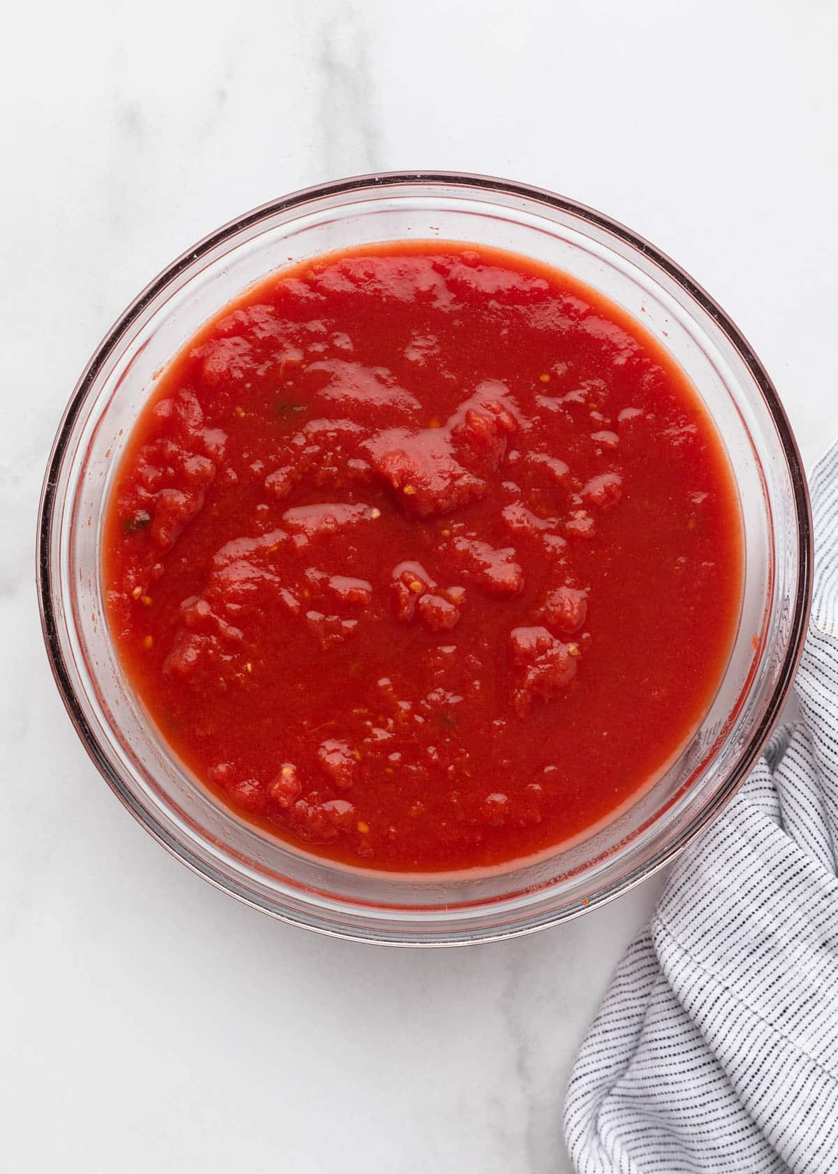 hand crushed plum tomatoes in a glass bowl on a white marble surface
