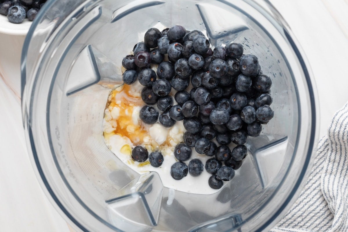 overhead of blueberries, honey, cottage cheese, and coconut cream in a blender canister