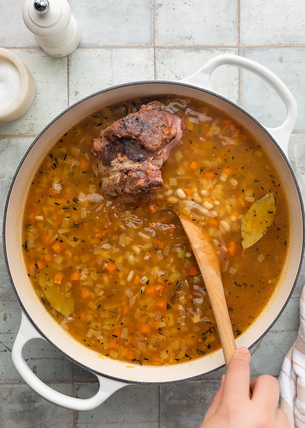stirring chicken stock and water into a pot of ham and bean soup with a wooden spoon