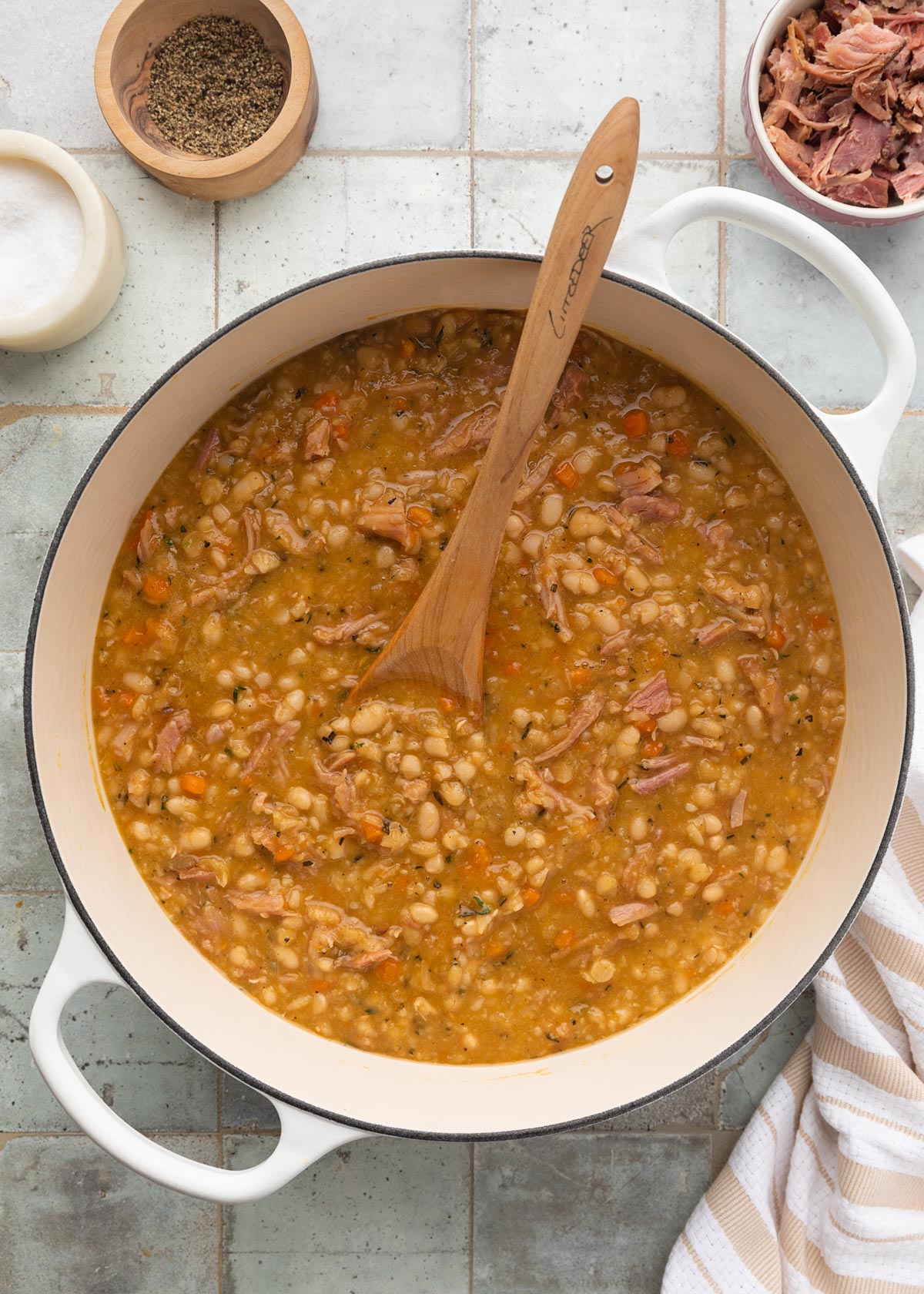 cooked ham and navy bean soup in a white enameled cast iron Dutch oven with a wooden spoon