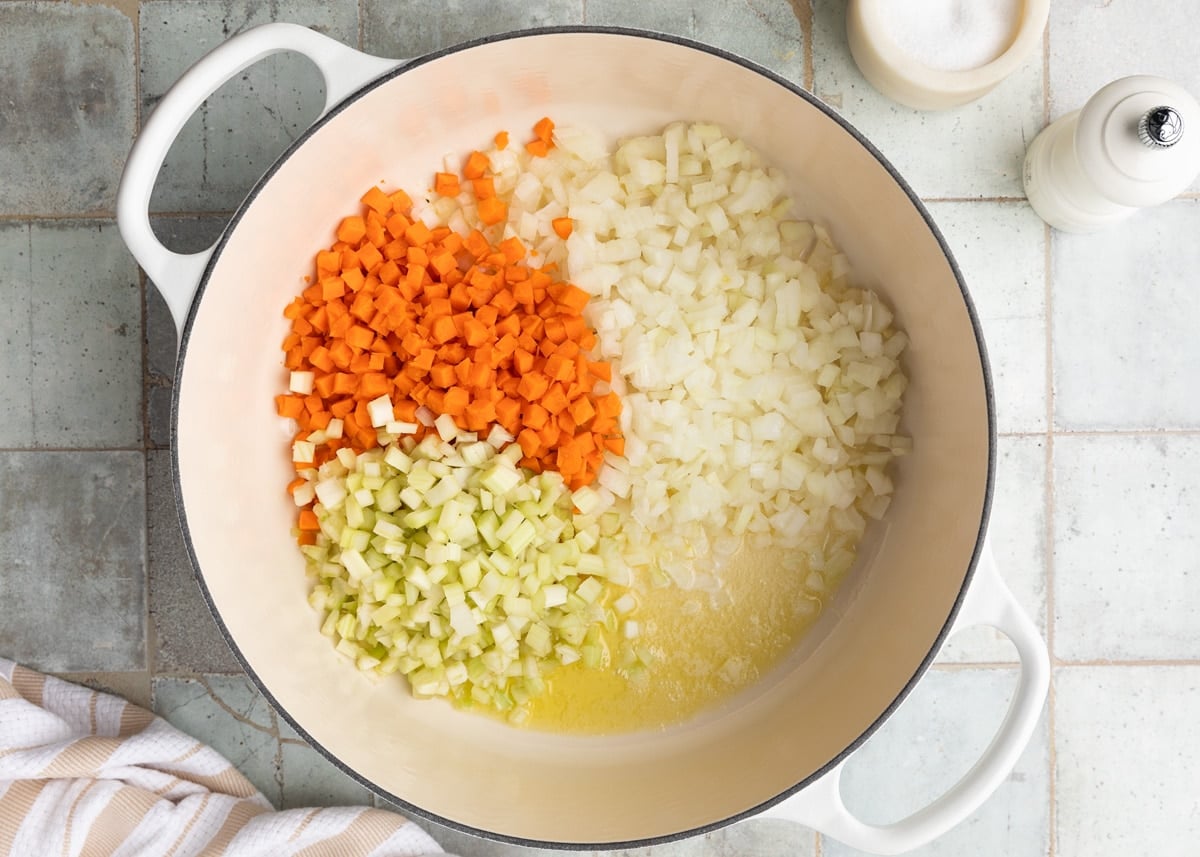 diced celery, carrots, and onions with butter and olive oil in a white enameled cast iron Dutch oven