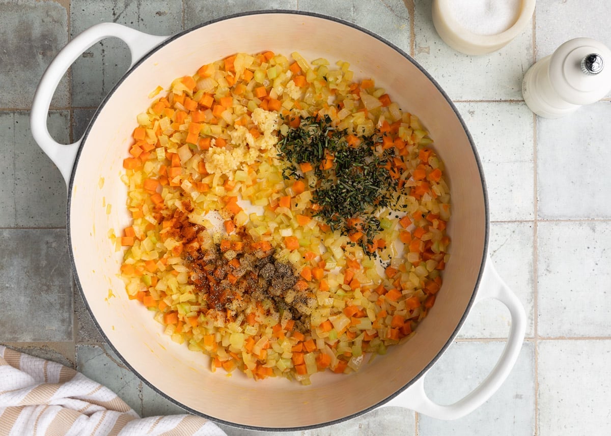 sauteed mirepoix in a white enameled cast iron Dutch oven with fresh herbs, paprika, and black pepper added