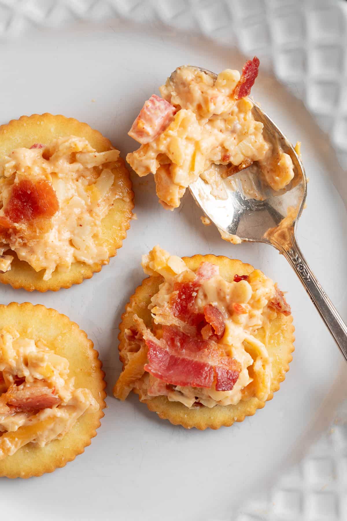 bacon pimento cheese on ritz crackers on a white plate with a silver spoon