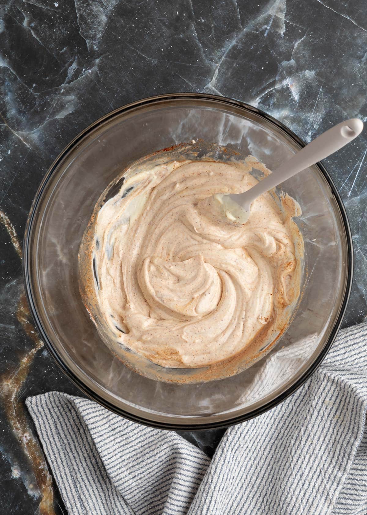 seasoned mayonnaise in a glass bowl with a rubber spatula on a black marble board