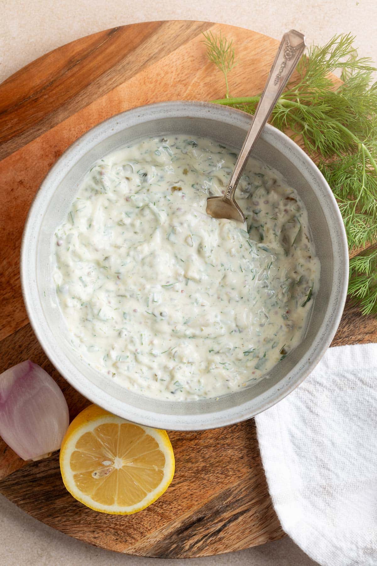 overhead of a bowl of mixed tartar sauce on a wooden board with a spoon