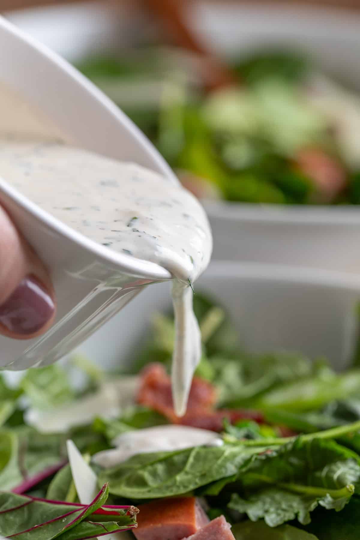 pouring dill ranch dressing over a spinach pea salad from a white cup