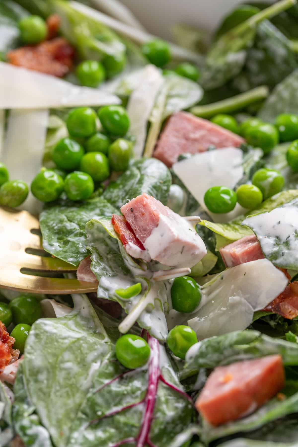 closeup of spinach and pea salad dressed with ranch dressing in a bowl with a fork