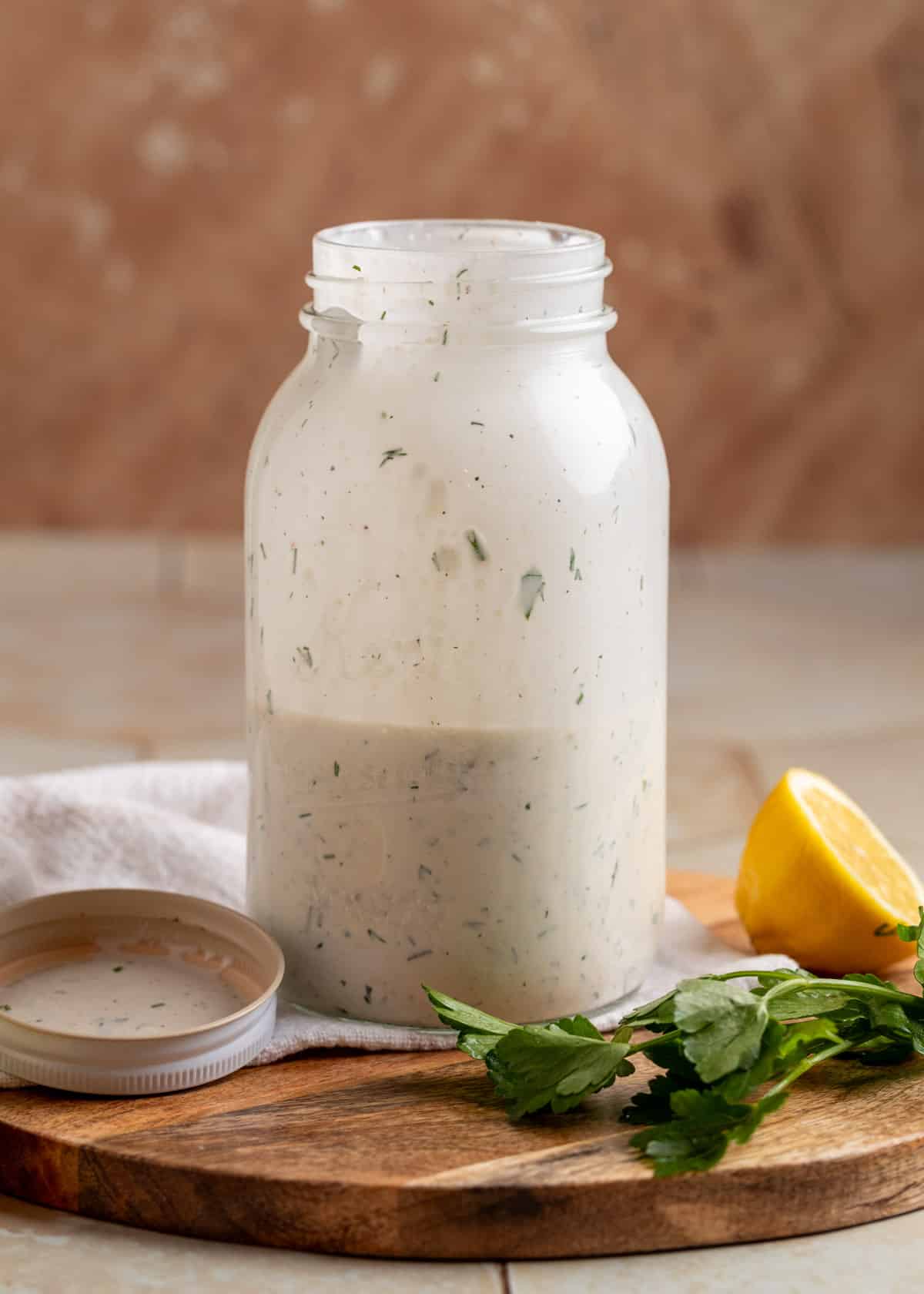 dill ranch dressing shaken in a mason jar on a wooden board next to dill and a lemon wedge