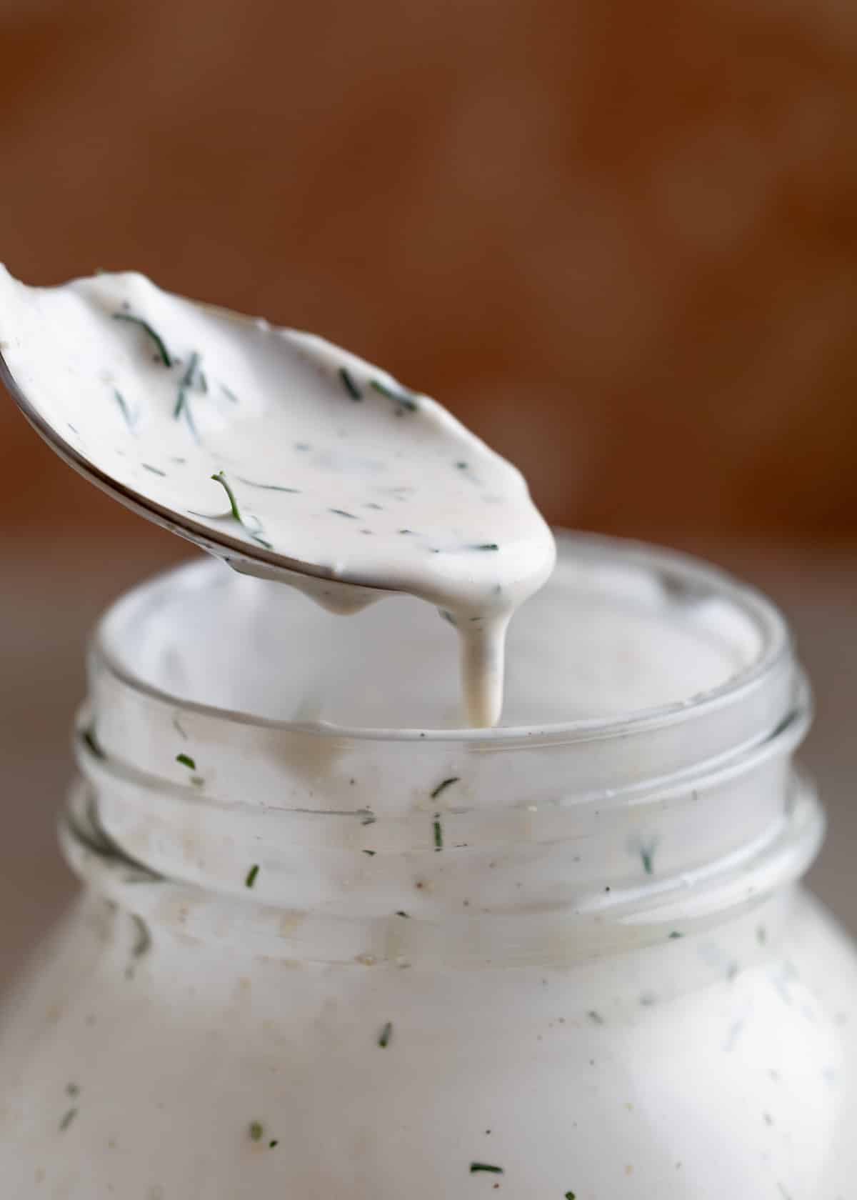 dill ranch dressing being drizzled from a spoon into a mason jar of the dressing