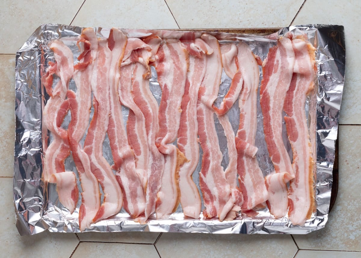overhead of raw bacon on a foil lined baking sheet
