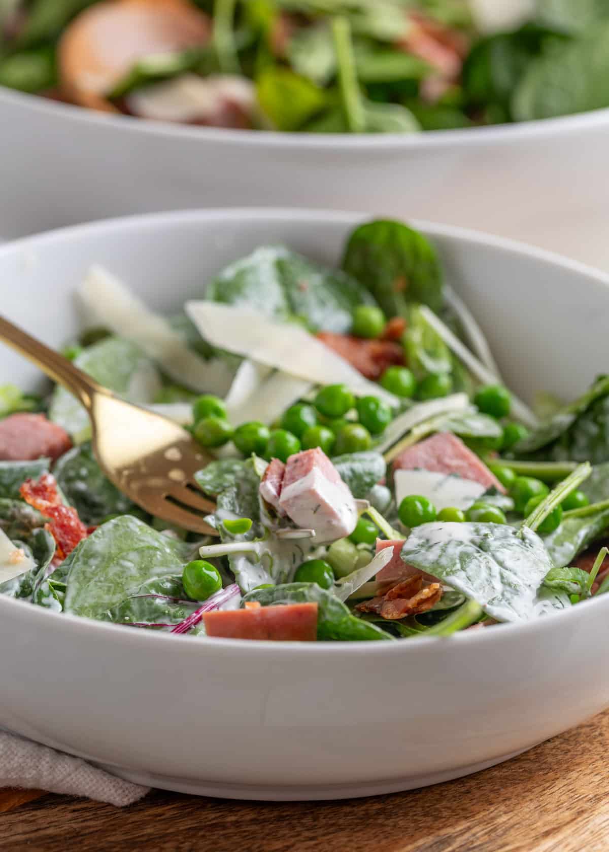 side view of spinach pea salad with dill ranch dressing in a white bowl with a gold fork
