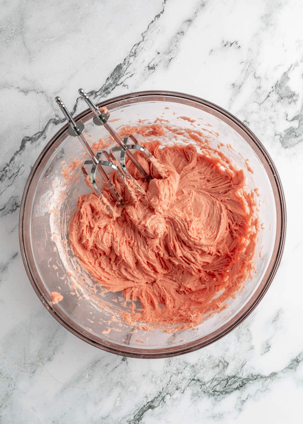 mixed strawberry chess bar dough in a glass bowl on a white marble board with stainless steel hand mixer beaters